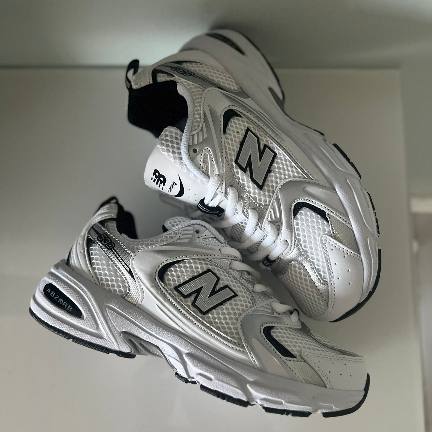 Zapatillas premium modelo 530 blanca con detalles gris y negros.