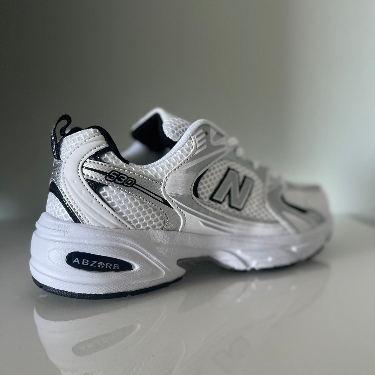 Zapatillas premium modelo 530 blanca con detalles gris y negros.